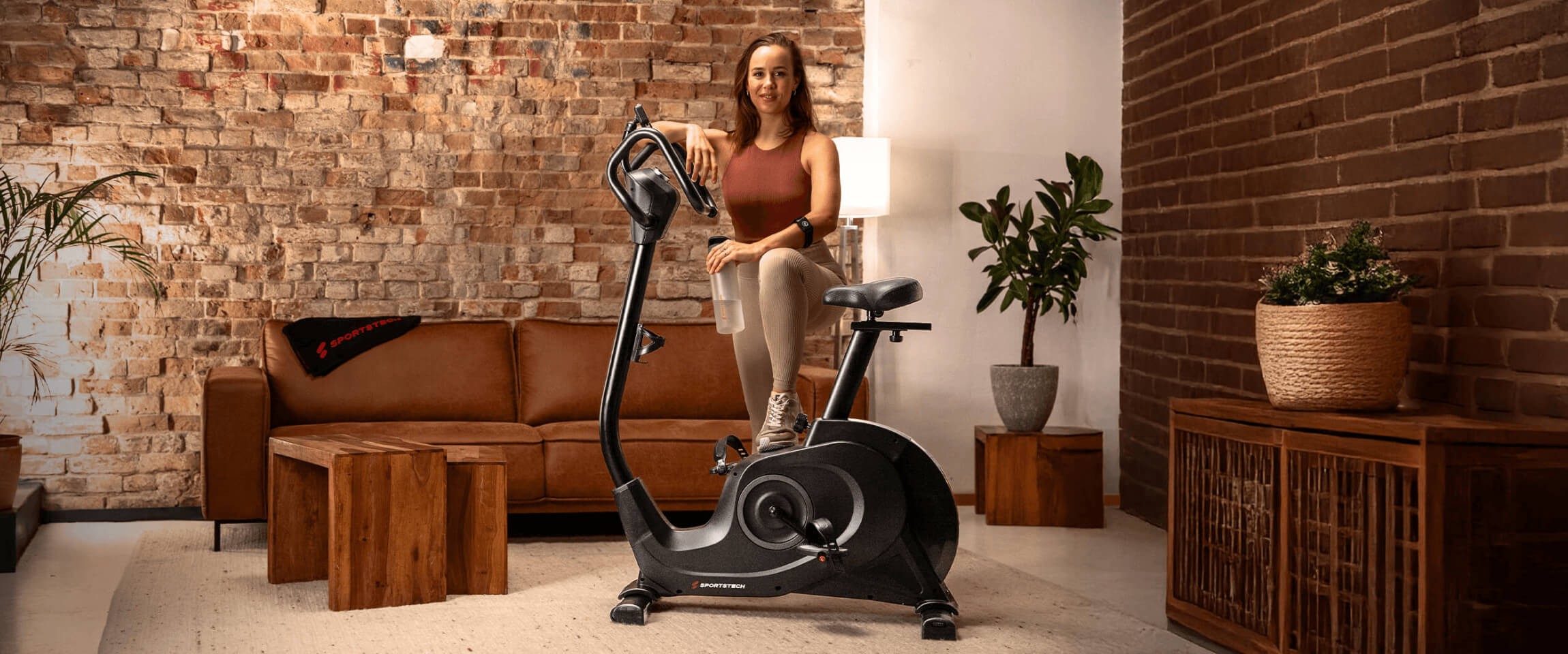 Eine Frau steht vor einem Ergometer in ihrem Wohnzimmer