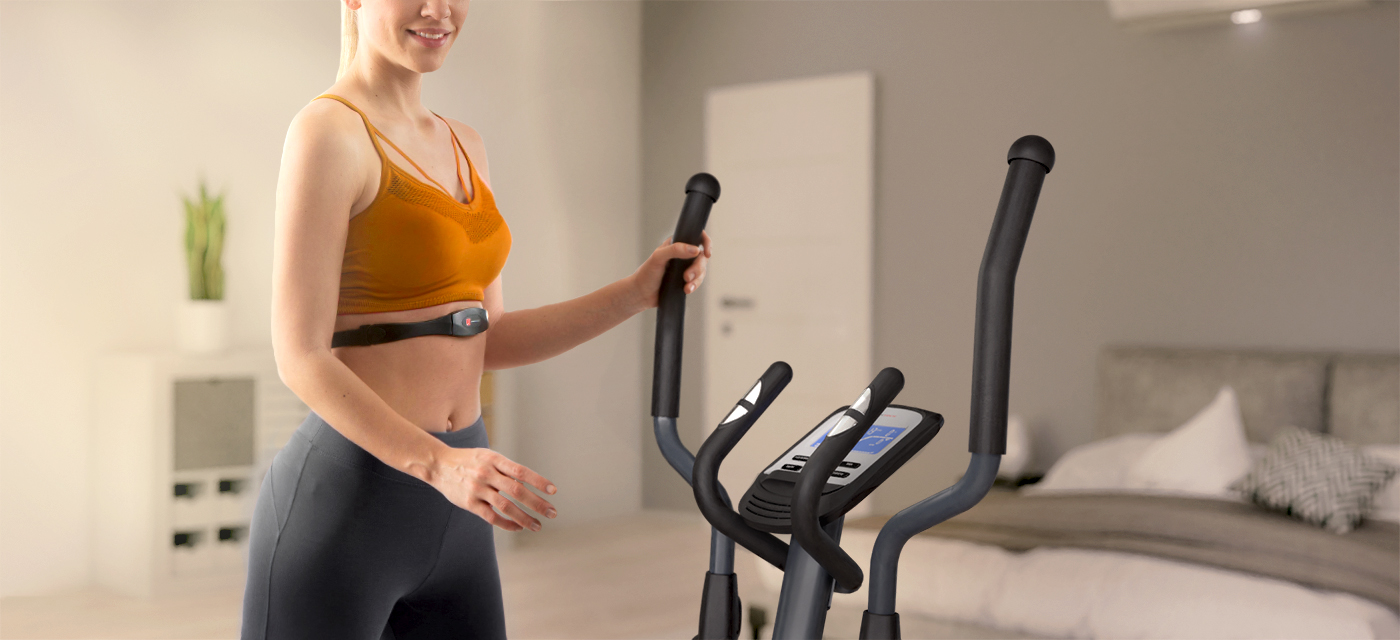 Integrierte Pulssensoren beim Crosstrainer CX625 von Sportstech Frau in Sportkleidung verwendet einen Pulsgurt zur Messung der Herzschläge beim Training mit dem Sportstech Crosstrainer CX625
