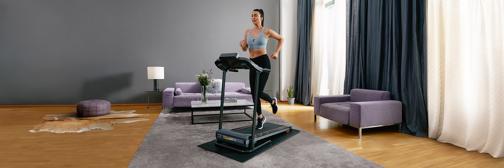 Schwarzes Laufband F10 Sportstech Frau in Sportbekleidung läuft auf schwarzem Laufband F10 im Wohnzimmer