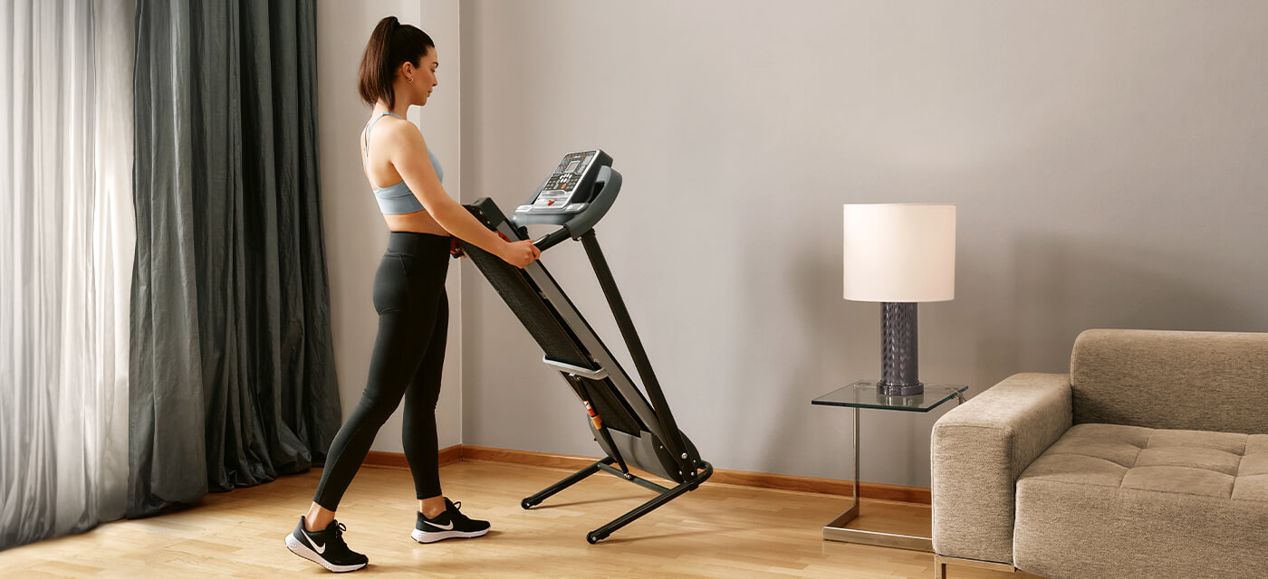 Schwarzes Laufband F10 Sportstech Frau in Sportkleidung klappt schwarzes Laufband F10 zusammen